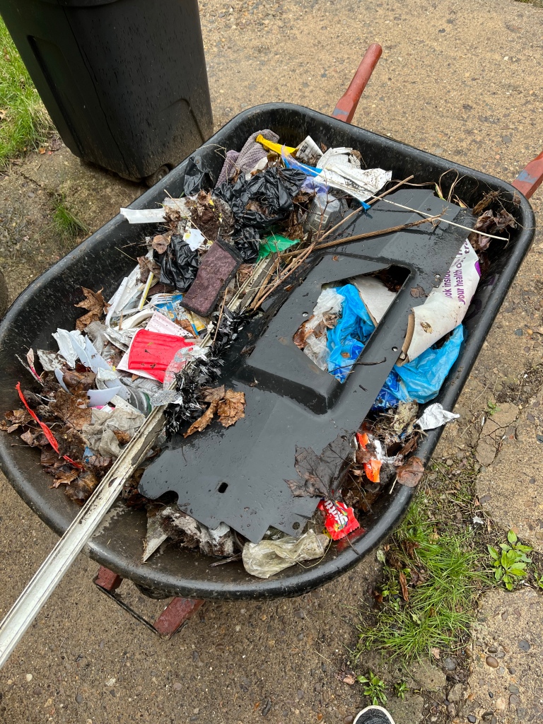 A wheelbarrow full of garbage. Various plastic bottles, plastic car parts, cigarette butts, shopping bags, paper pulp, aluminum cans, and more. 